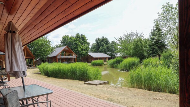 Une terrasse en bois avec des meubles d’extérieur, un étang et une végétation luxuriante tout autour.