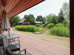 A wooden deck with outdoor furniture, a pond, and surrounding greenery. - Sunnyside Lodge (Lincoln)