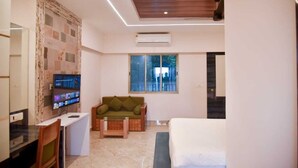 Ein modernes Hotelzimmer mit Holzbalkendecke, einem an der Wand montierten Flachbildfernseher, einem grünen Sofa, einem Bett und einem Fenster mit Blick nach außen.
