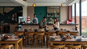 Ein Restaurant mit Holztischen und -stühlen, einer Bar und einer grünen Wand mit Regalen.