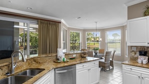 A modern kitchen with granite countertops, stainless steel appliances, and large windows offering views of the outdoors.