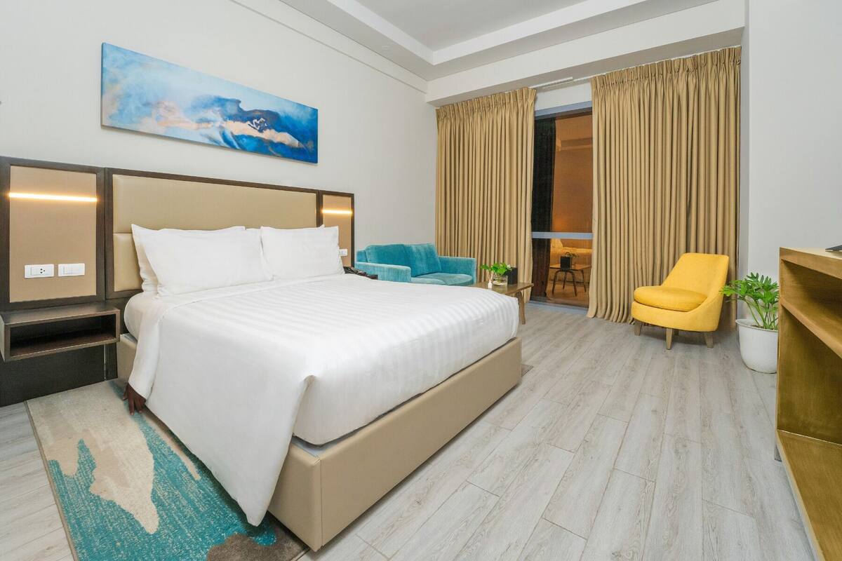 A hotel room with a large bed, a desk, a chair, and a view of the outside.