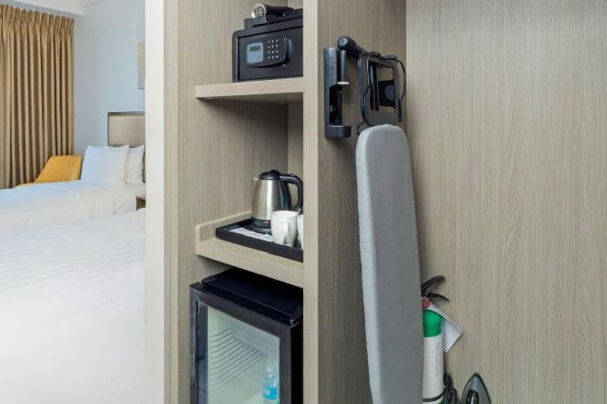 A hotel room with a bed, a minibar, a coffee maker, a microwave, and a ironing board.
