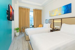 Habitación de hotel con dos camas, televisión, un cuadro y vista a la ciudad.