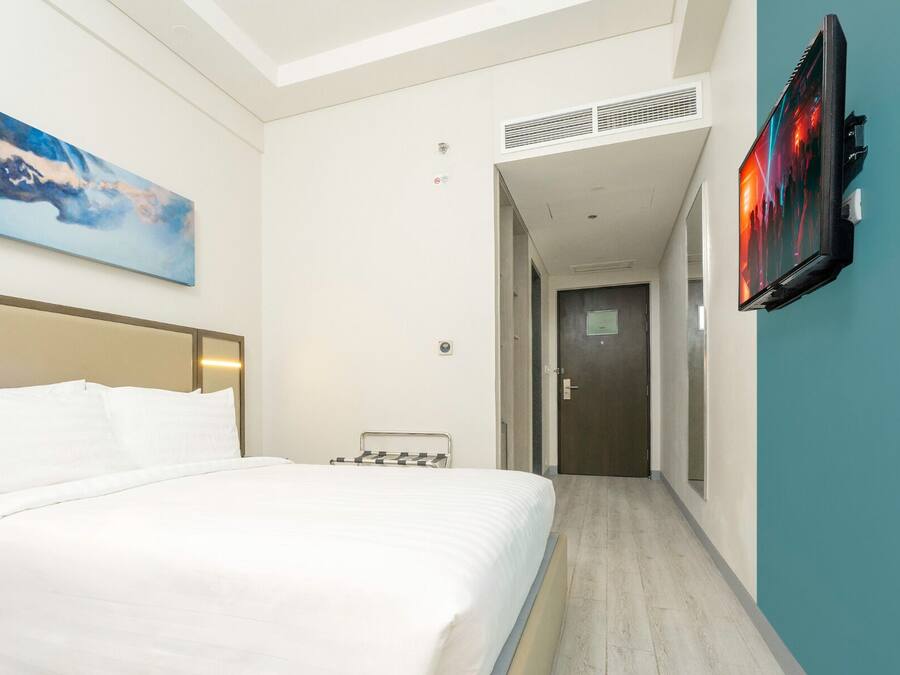 A hotel room with a bed, a painting, a television, and a hallway leading to another room.