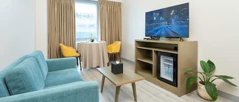 Un salon moderne avec un canapé bleu, une table basse en bois, un téléviseur à écran plat fixé sur un meuble en bois et une plante en pot.
