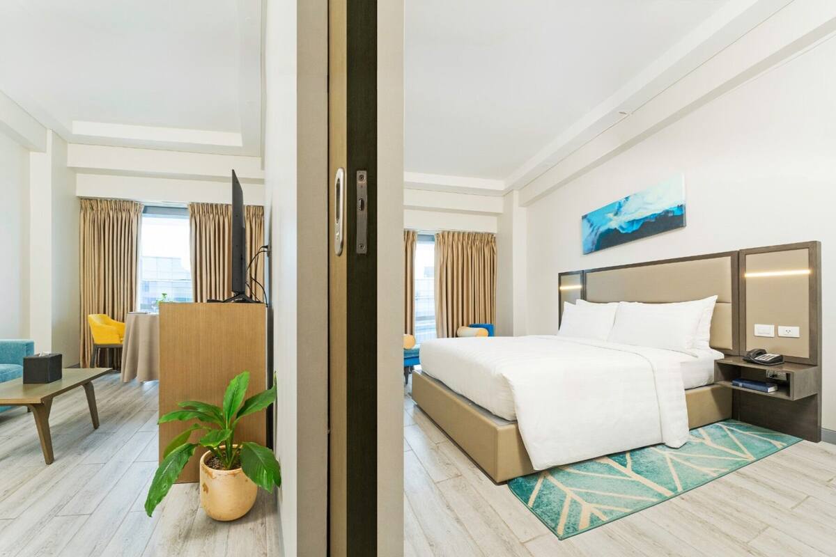 A hotel room with a bed, bedside table, lamp, and a potted plant.