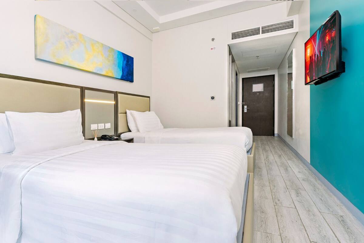 A hotel room with two beds, a large abstract painting, a television, and a hallway leading to another room.
