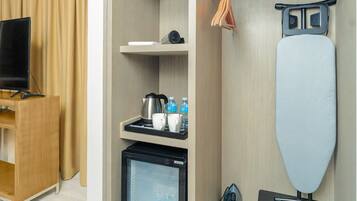 Habitación de hotel pequeña con televisión de pantalla plana, refrigerador, cafetera y tabla de planchar.