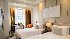 Ein Hotelzimmer mit zwei Betten, einem Schreibtisch, einem Stuhl, einer Lampe und einem großen, abstrakten Gemälde an der Wand.