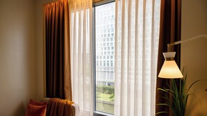 Ein Hotelzimmer mit großem Fenster, einer Lampe, einer Couch und einer Pflanze.