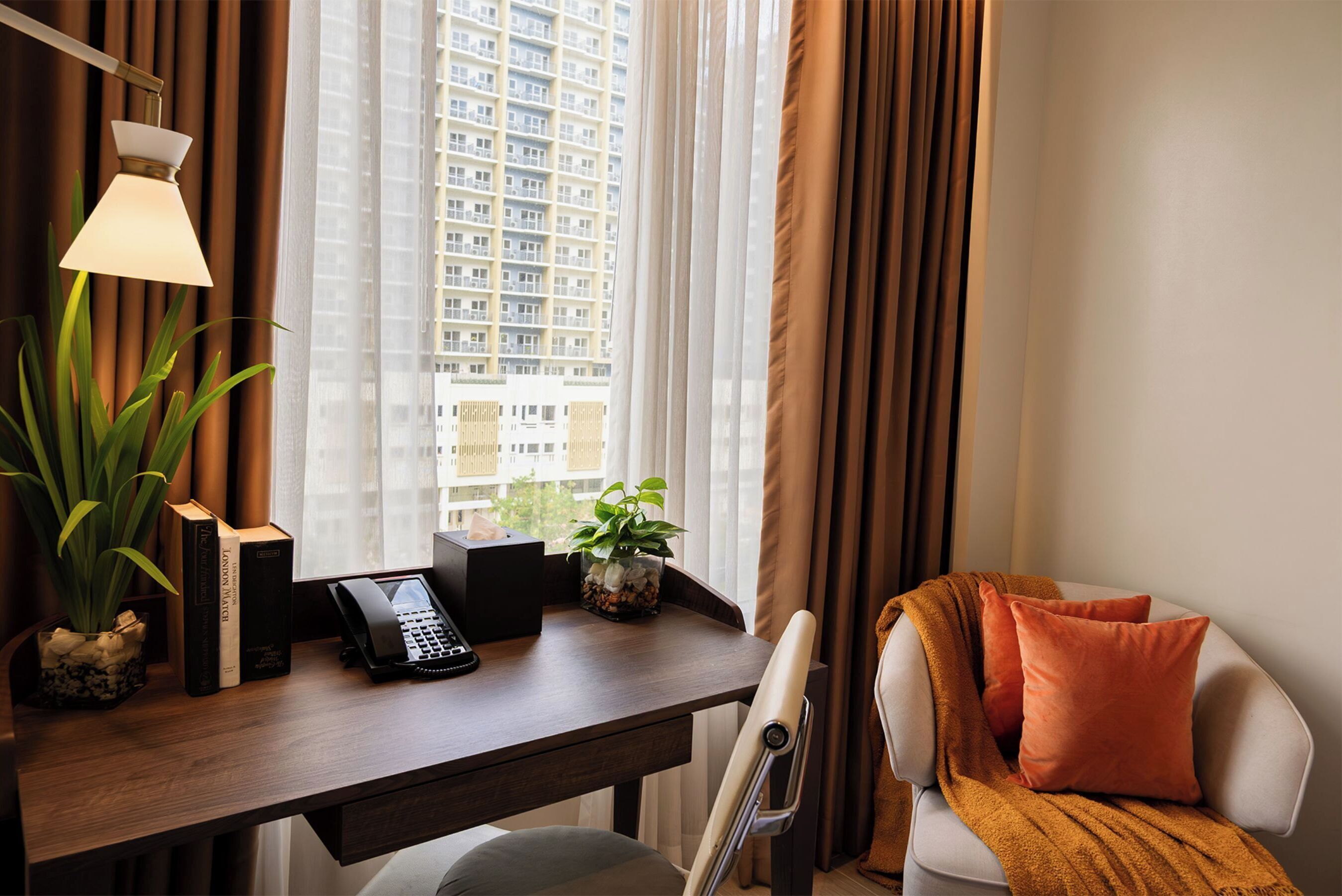 Une chambre d’hôtel équipée d’un bureau, d’un téléphone, d’une plante et offrant une vue sur un immeuble de grande hauteur.
