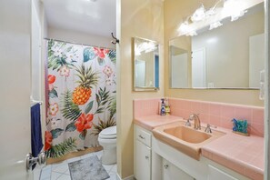 Une salle de bain équipée de toilettes, d’un lavabo et d’un rideau de douche orné d’un motif floral tropical.
