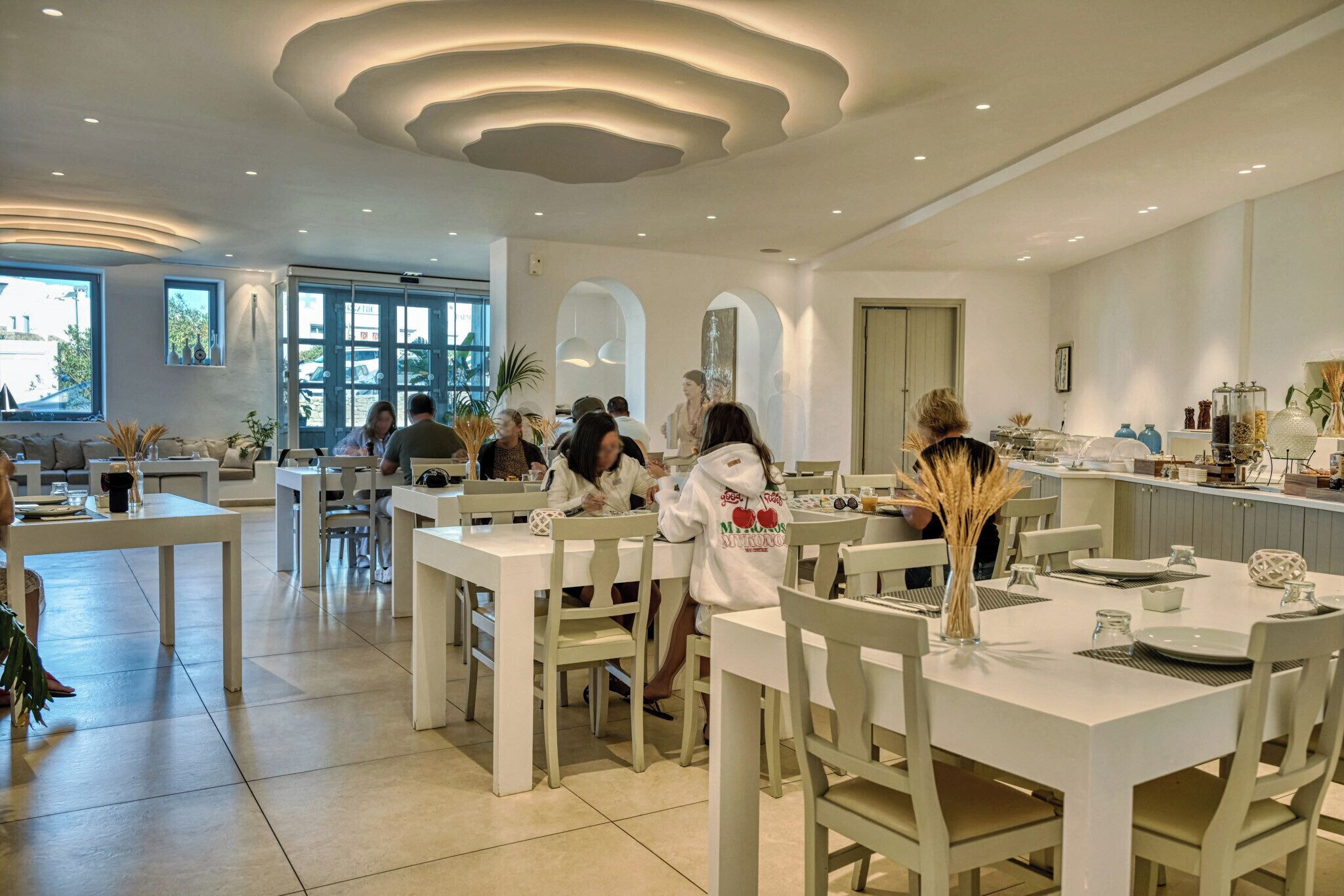 A modern dining area with white furniture, a central bar, and large windows allowing natural light.
