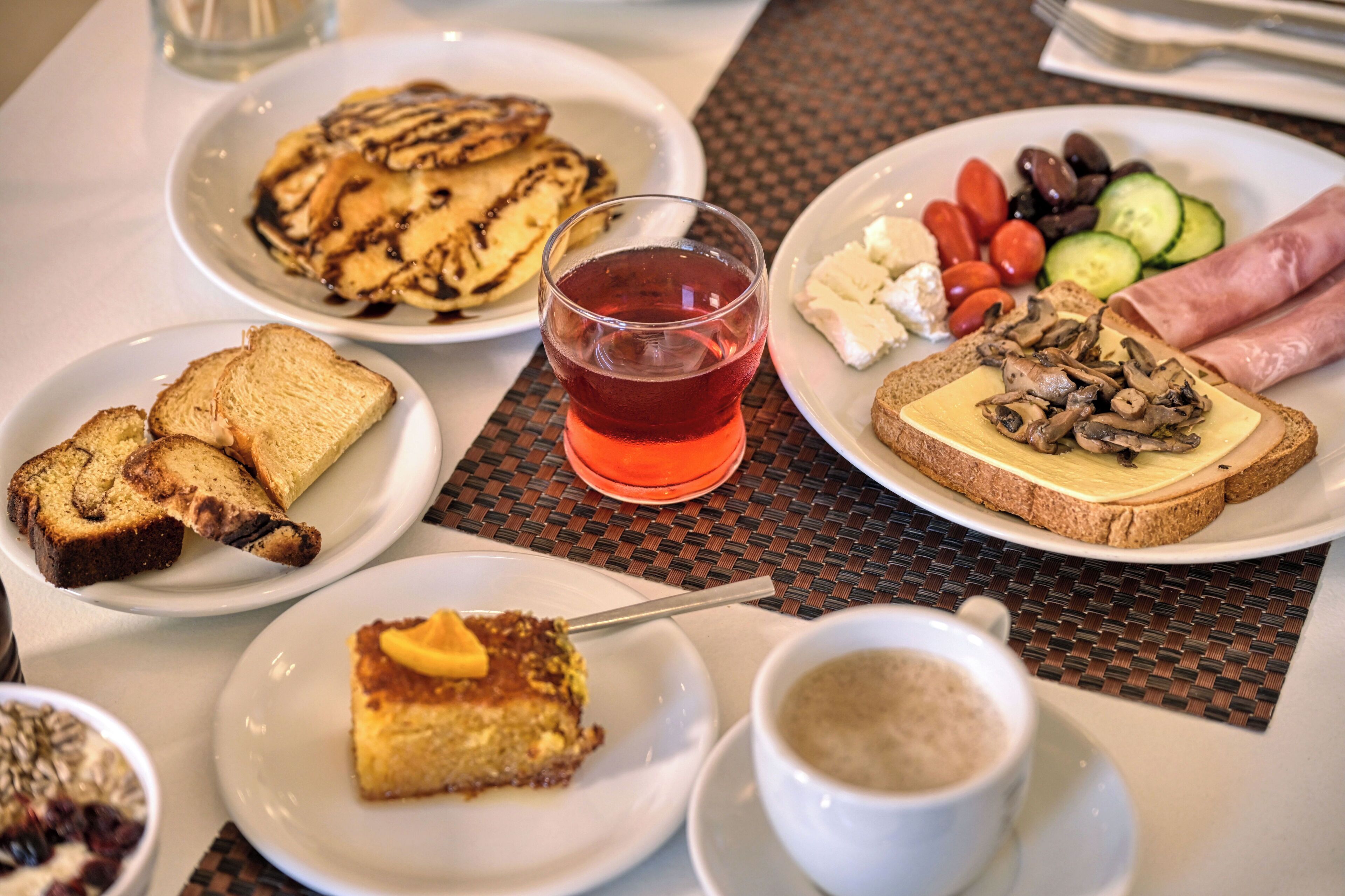 A table with plates of food, a glass of red drink, and a cup of coffee.