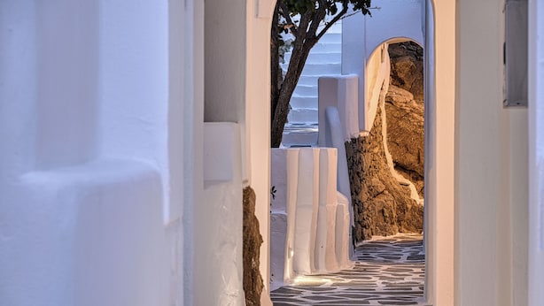 Un pasillo estrecho, con paredes blancas y suelo de piedra, que conduce a una zona rocosa.