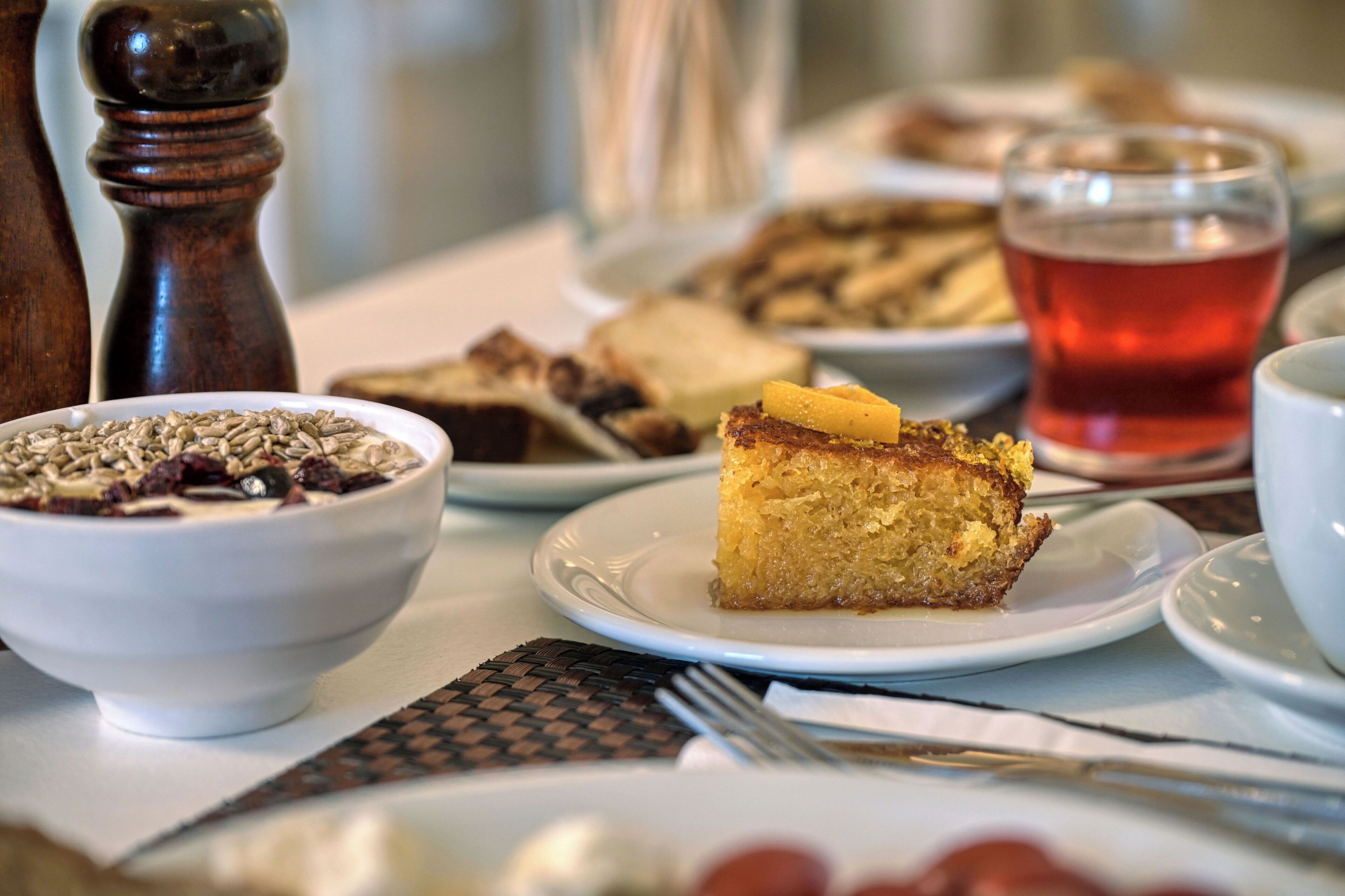 Una mesa con una rebanada de pastel, un tazón de cereal y un vaso de bebida roja.