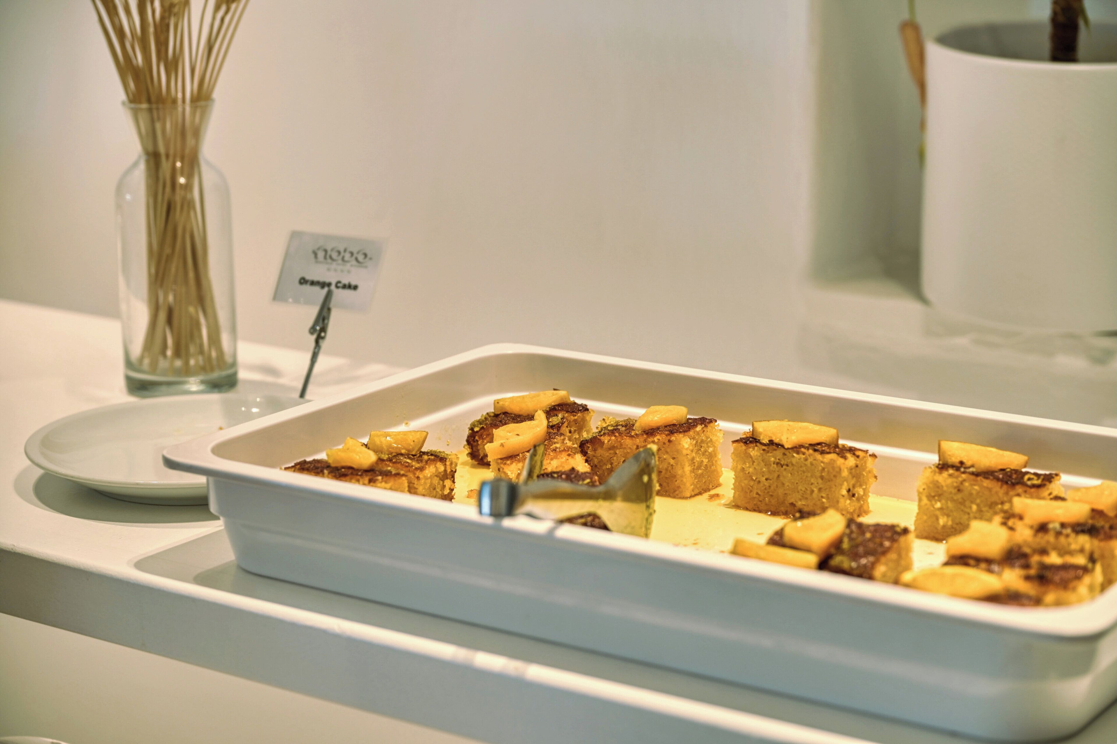 Un plateau contenant divers aliments est posé sur une table, et une étiquette indique : « Gâteau à l’orange ».