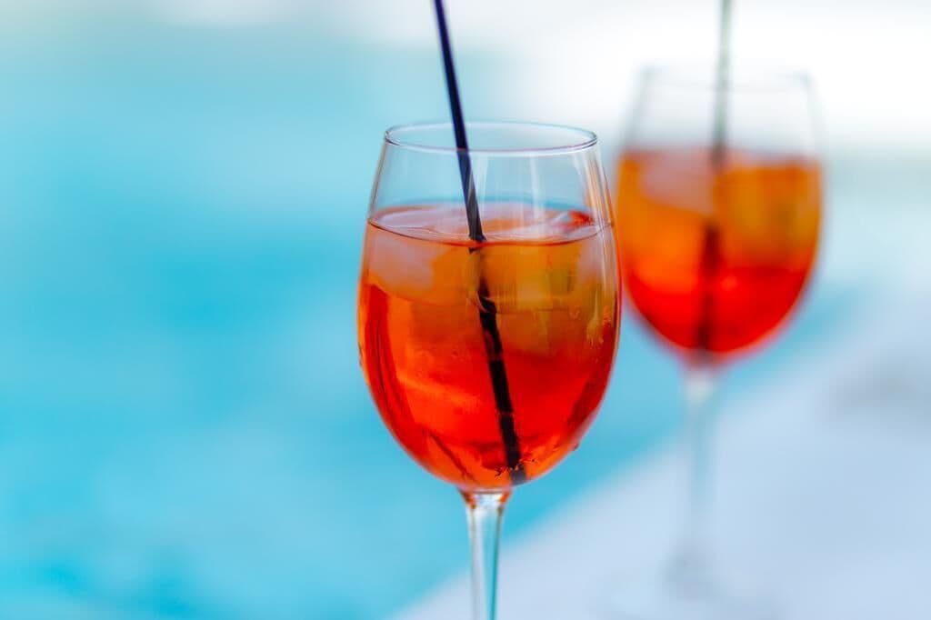 Two glasses of red beverage with a straw, set against a blue background.