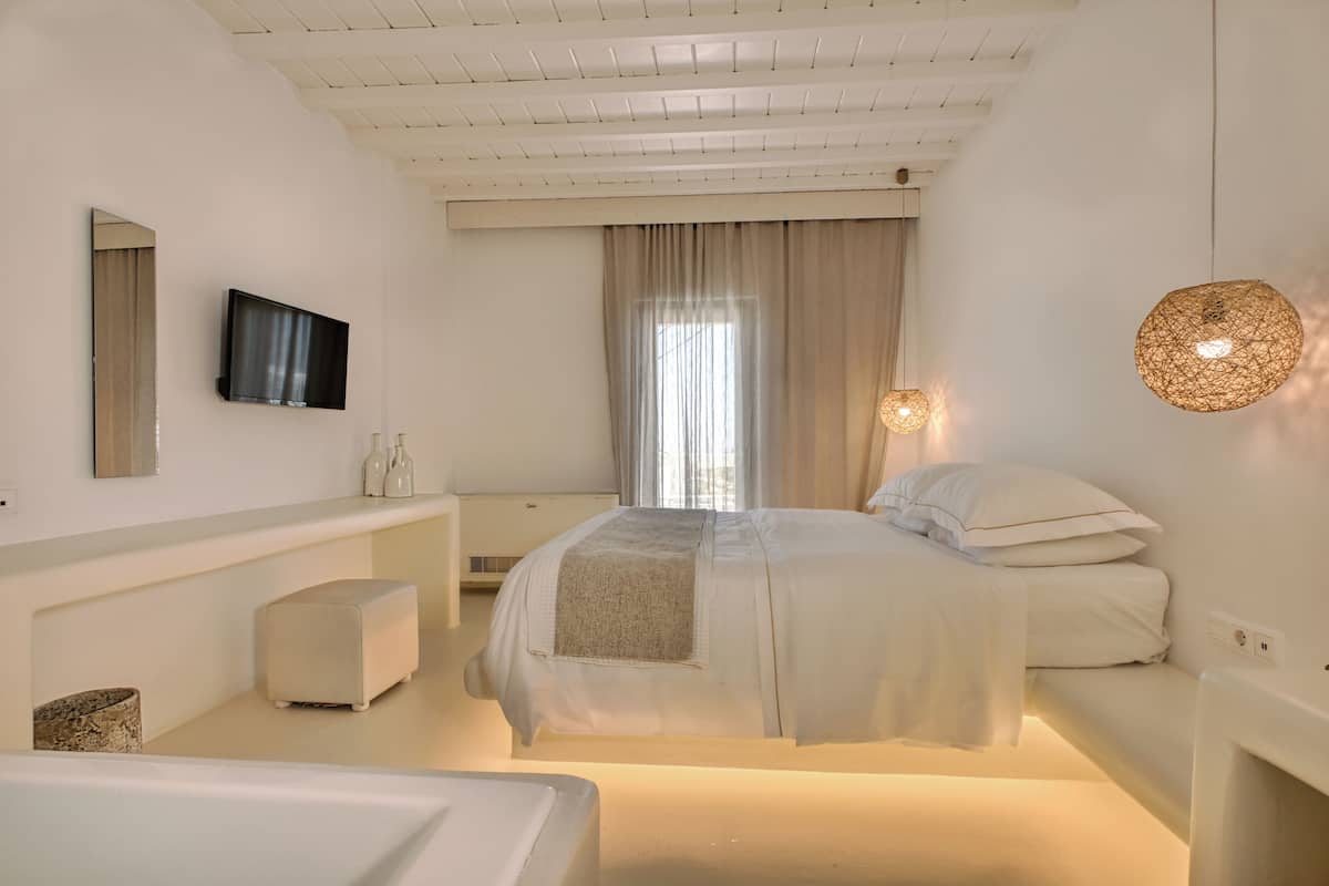 Une chambre moderne avec un lit, des tables de chevet, une télévision et une grande fenêtre avec des rideaux.