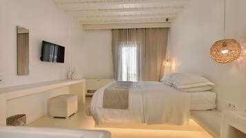 Un dormitorio moderno con cama, mesitas de noche, televisor y un amplio ventanal con cortinas.
