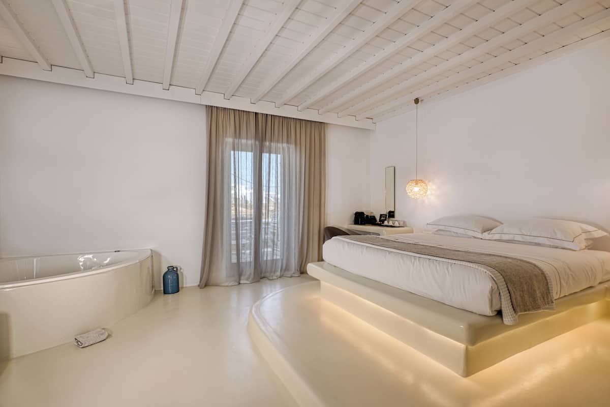 Une chambre moderne avec un grand lit, une baignoire et une grande fenêtre avec des rideaux.