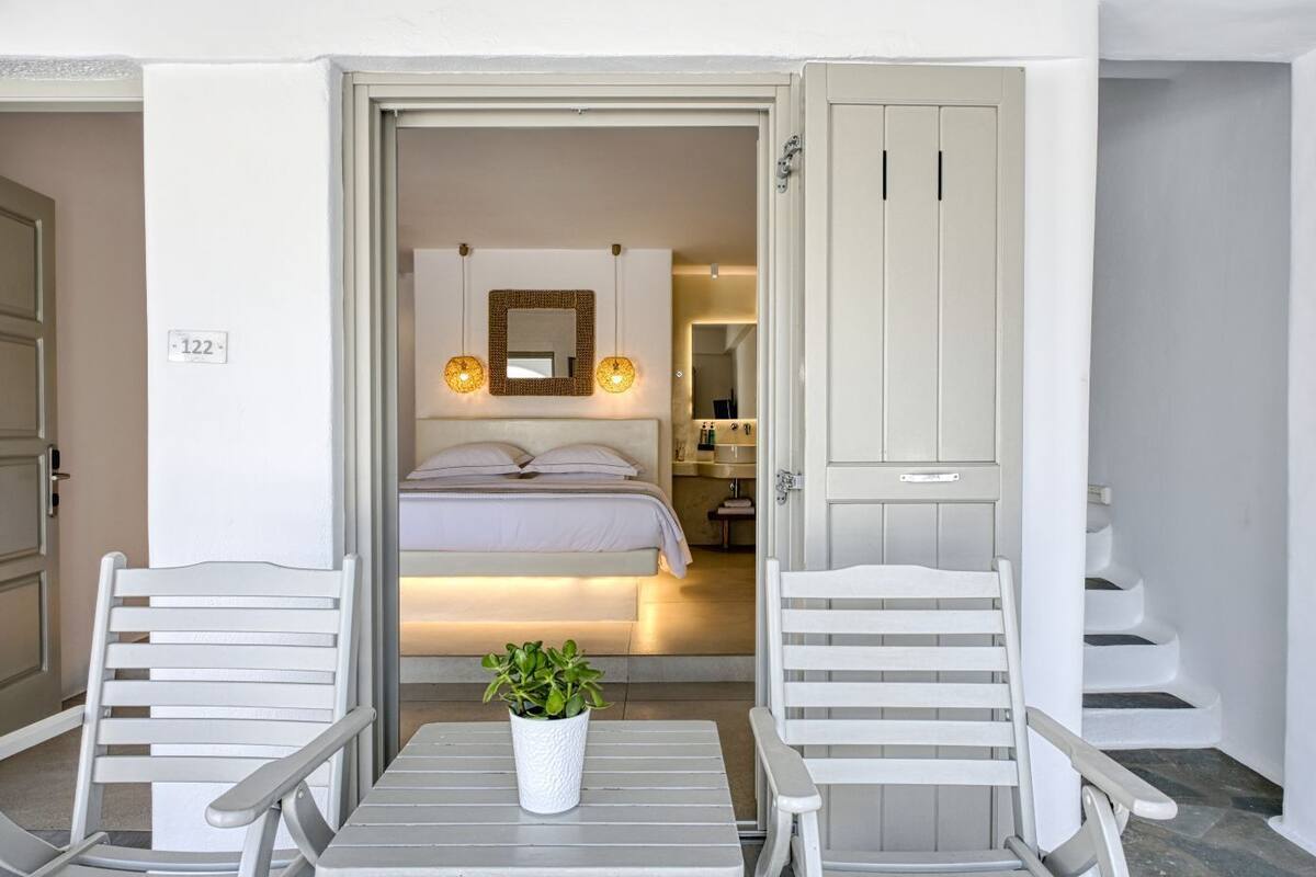Une chambre à coucher avec un lit, des lampes de chevet, une plante en pot et une salle de bain visible à travers une porte ouverte.