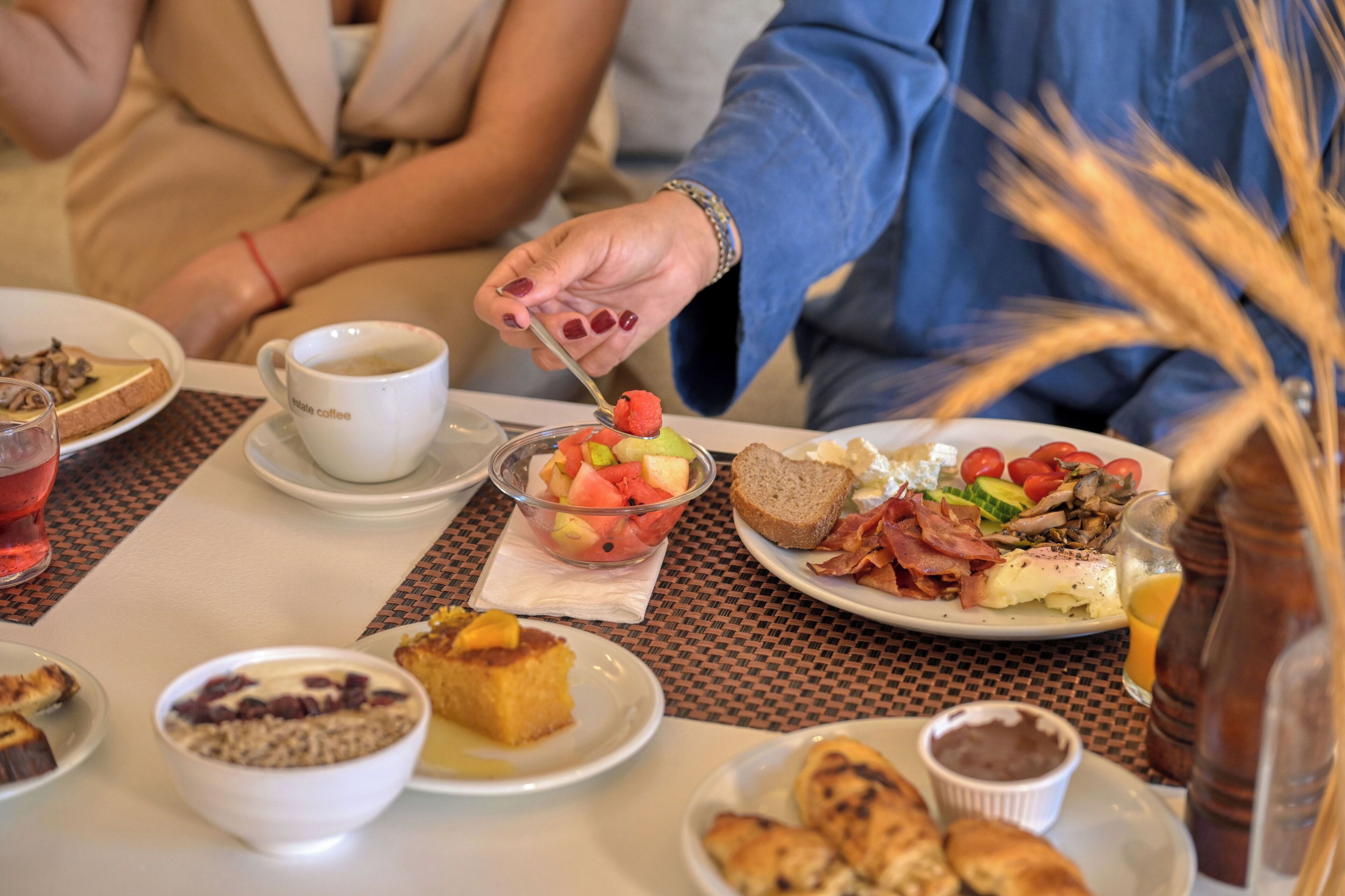Une table dressée pour le petit-déjeuner avec différents plats, une tasse de café et une personne qui mange.