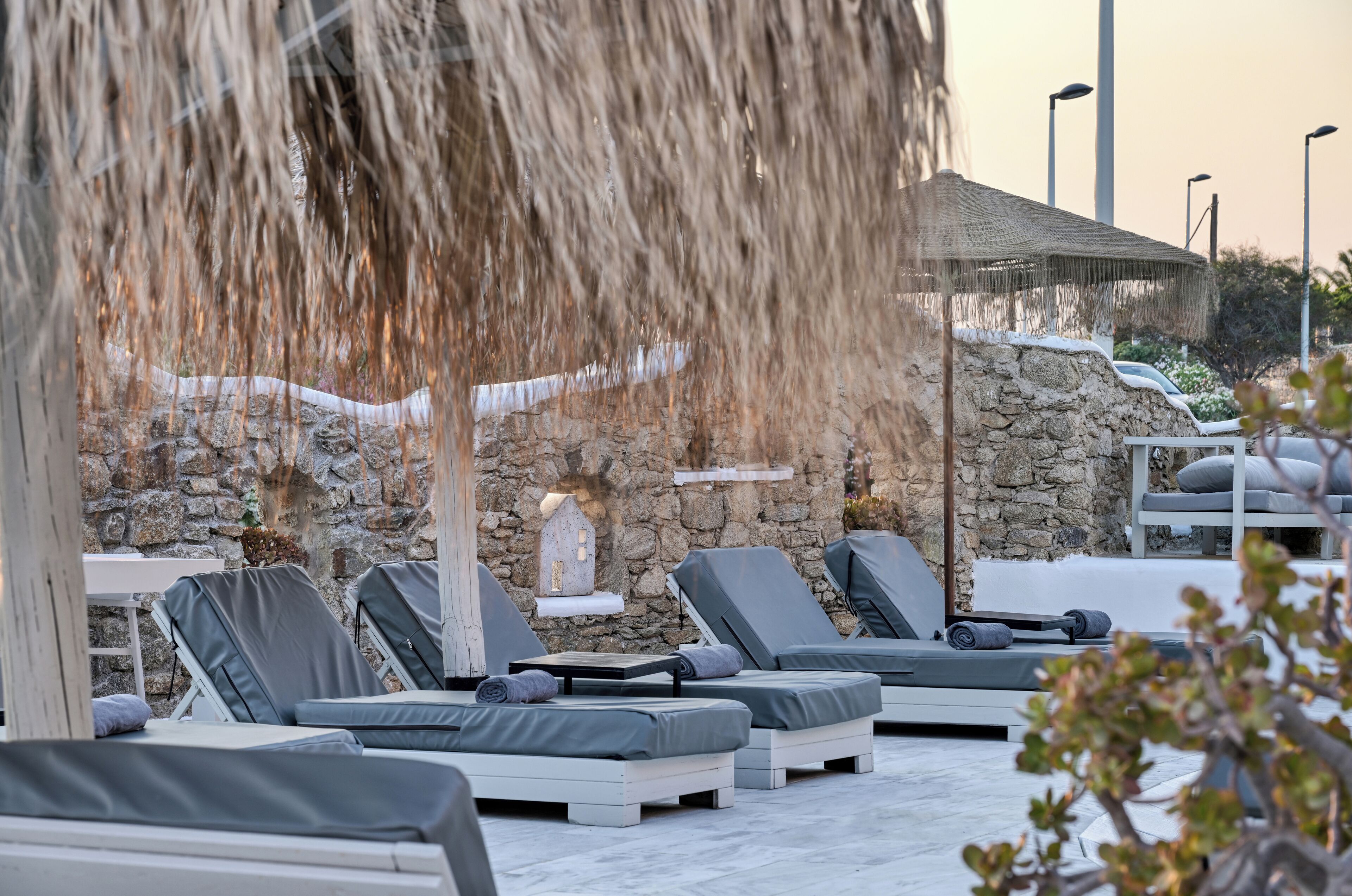 Un espacio lounge al aire libre iluminado por el sol, con paredes de piedra, sillones de descanso y una fuente de agua.