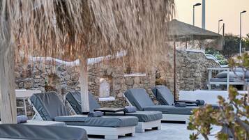 Un espacio lounge al aire libre iluminado por el sol, con paredes de piedra, sillones de descanso y una fuente de agua.