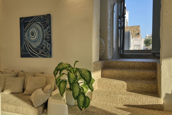 A living room with a beige sofa, a potted plant, and a spiral staircase leading to an outdoor area. - Nodo Hotel (Mykonos)
