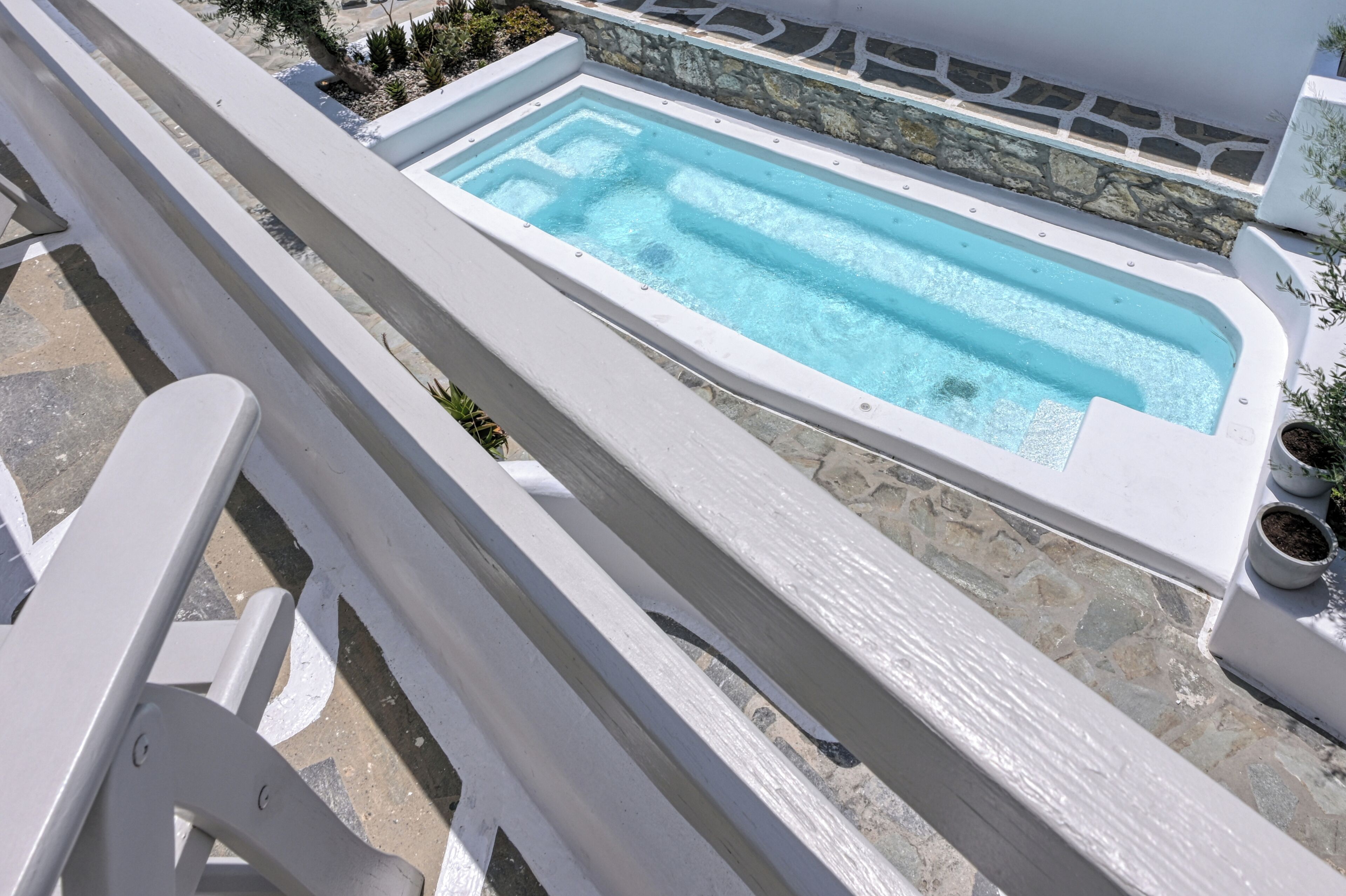 Una piscina rectangular con borde de piedra, rodeada por una barandilla blanca y plantas en macetas.
