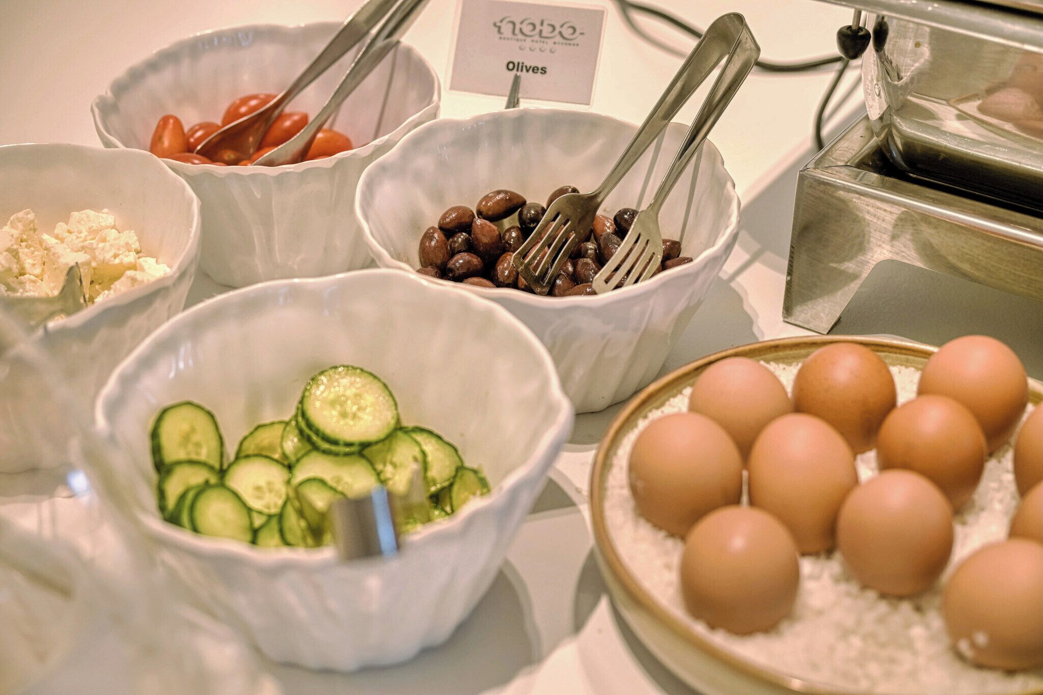 A buffet with various food items including olives, cucumbers, eggs, and tomatoes.