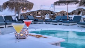 Zona de piscina con sillas de descanso y sombrillas, un muro de piedra y dos bebidas sobre una mesa.