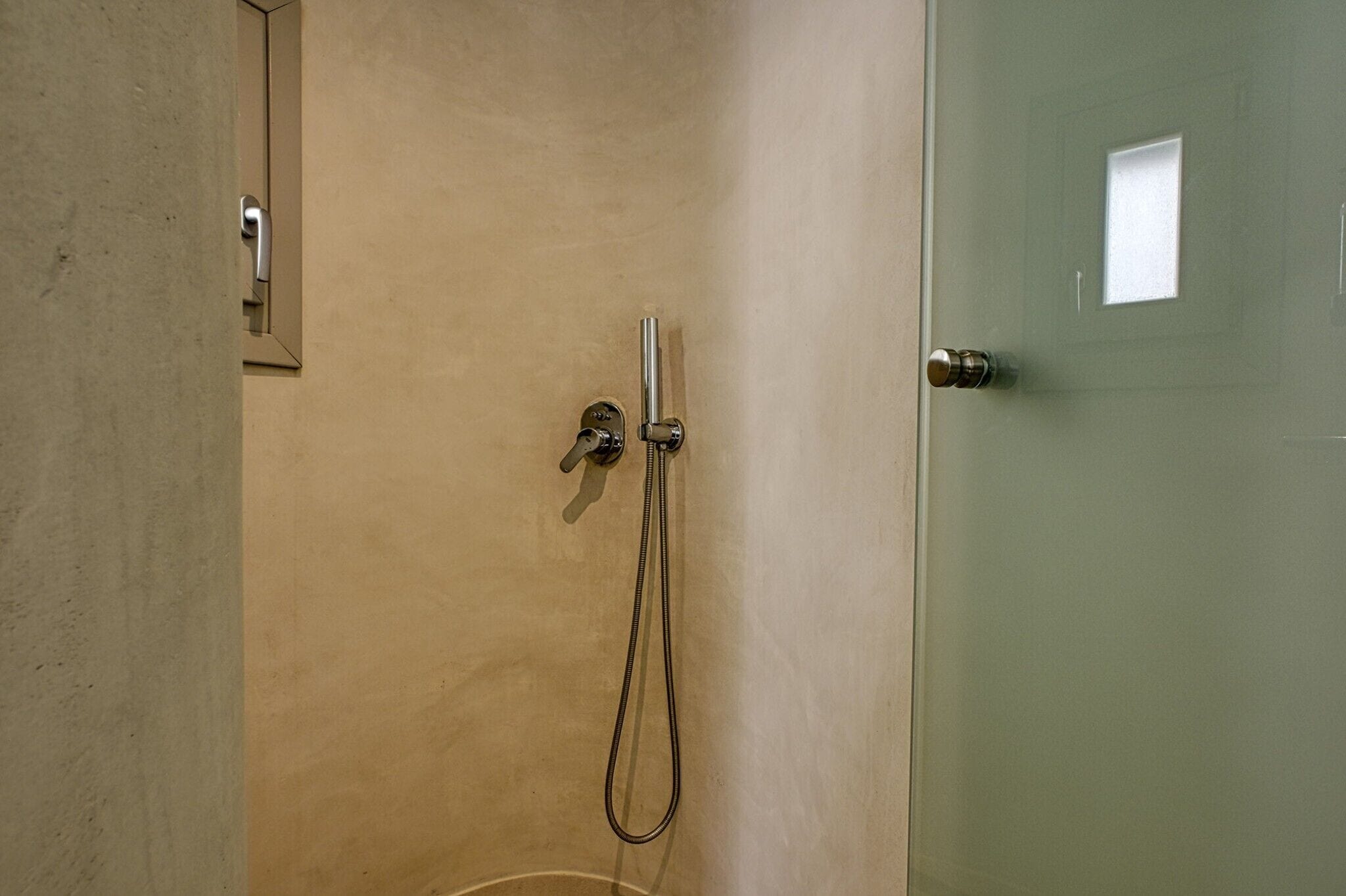 A shower with a handheld showerhead and a wall-mounted faucet.