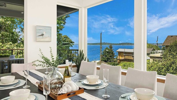 Un coin repas avec une table dressée pour six personnes, offrant une vue panoramique sur la mer et une île lointaine.