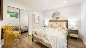 Ein Schlafzimmer mit Bett, Nachttisch, Sessel mit Decke, Spiegel und Kleiderschrank.