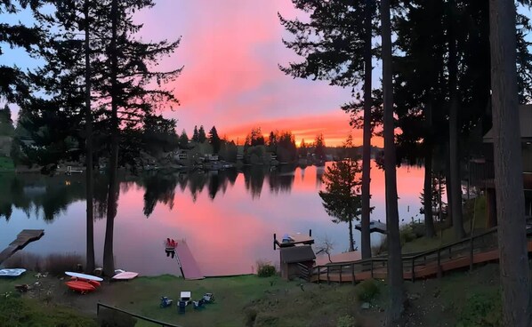 A lakeside view with a sunset, docked boats, and a small building.