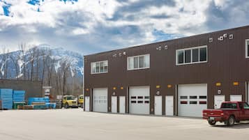 A large industrial building with multiple garage doors, a red pickup truck parked in front, and a mountainous background.