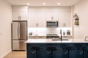 Una cocina moderna con armarios blancos, electrodomésticos de acero inoxidable, una isla central con taburetes y un microondas sobre el horno.