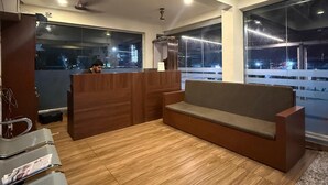 A modern waiting area with a wooden floor, a sofa, a reception desk, and large windows offering a view of the outside. - Indeo Residency (Kanayannur)