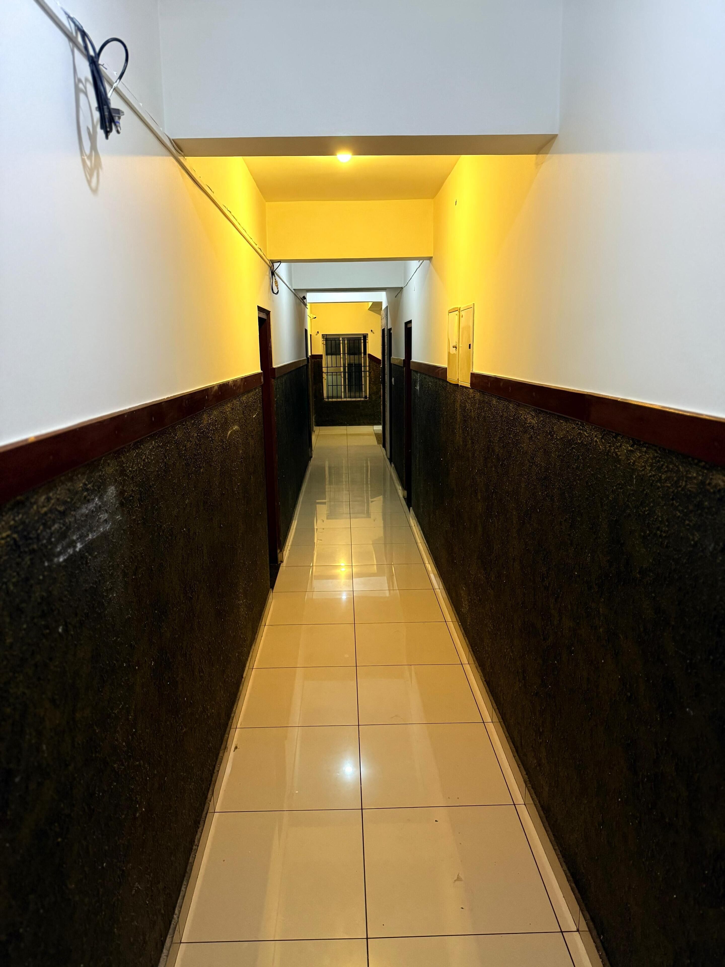 Un pasillo con piso de baldosas, paredes con una combinación de colores oscuros y claros, y una luz en el techo.