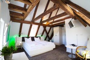 Une chambre avec un grand lit, une table de chevet, une petite table, une chaise et une plante verte.