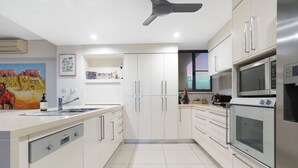 A modern kitchen with white cabinets, stainless steel appliances, and a ceiling fan.