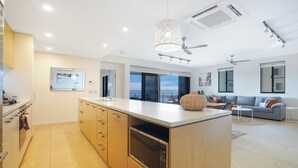 Une cuisine moderne dotée d’un grand îlot central, d’appareils électroménagers intégrés et offrant une vue sur l’extérieur.