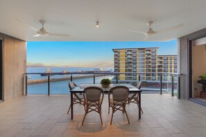 Ein Balkon mit Tisch und Stühlen, Blick auf einen Hafen und ein Hochhaus im Hintergrund.