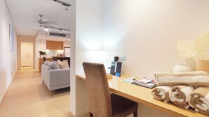 Una habitación de hotel moderna con un escritorio de madera, un sofá gris y un área de comedor al fondo.