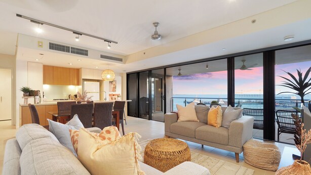 Un amplio salón con sofá, reposapiés y vistas al mar a través de amplios ventanales.
