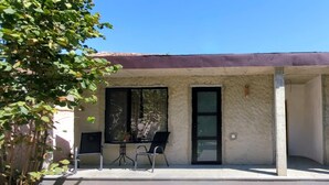 Un bâtiment doté d’un patio couvert, de deux chaises, d’une table et d’une porte.