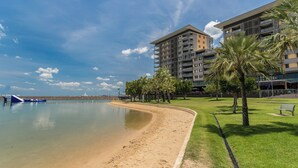 Ein Strandhotel mit Sandstrand, Palmen und modernen Gebäuden im Hintergrund.